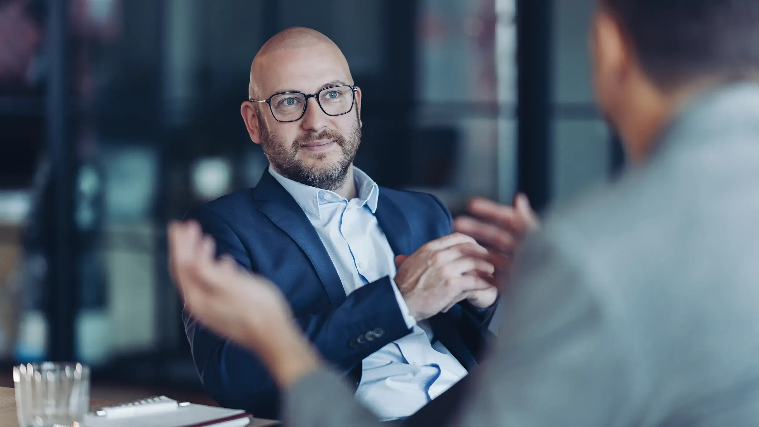 A professional consultant wearing glasses listening intently during a corporate meeting.