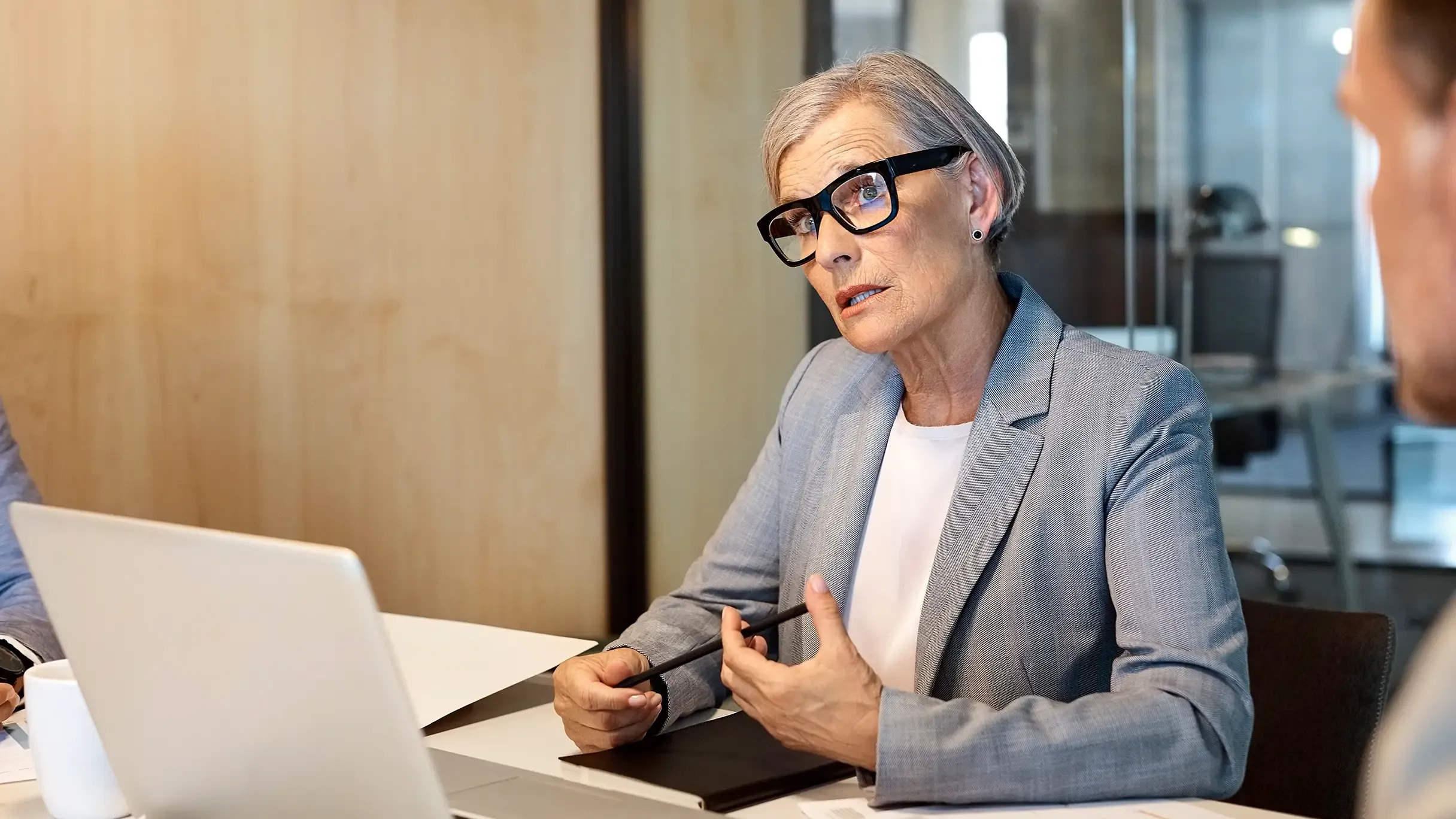 A professional woman with grey hair and glasses in an office setting.