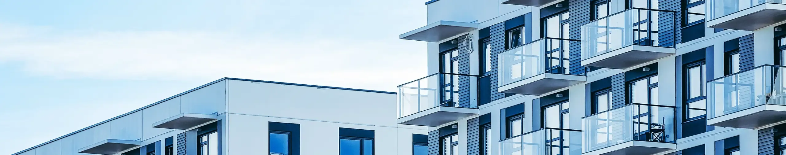 Modern apartment buildings with white facades and glass-fronted balconies under a bright blue sky.