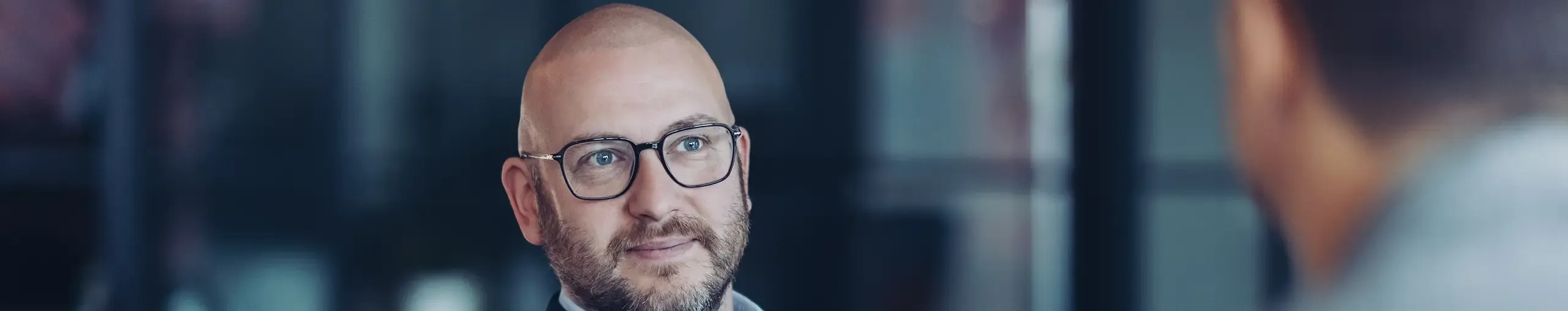 A professional consultant wearing glasses listening intently during a corporate meeting.