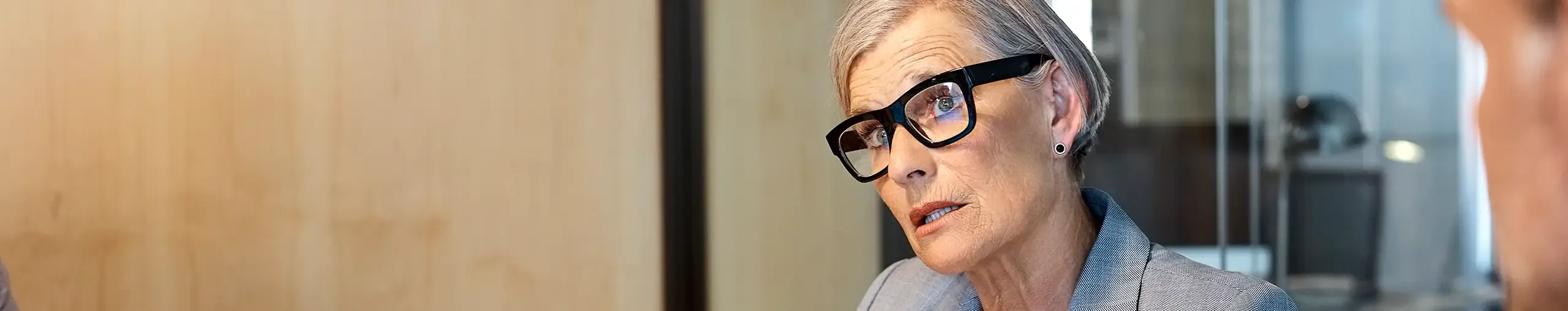 A professional woman with grey hair and glasses in an office setting.